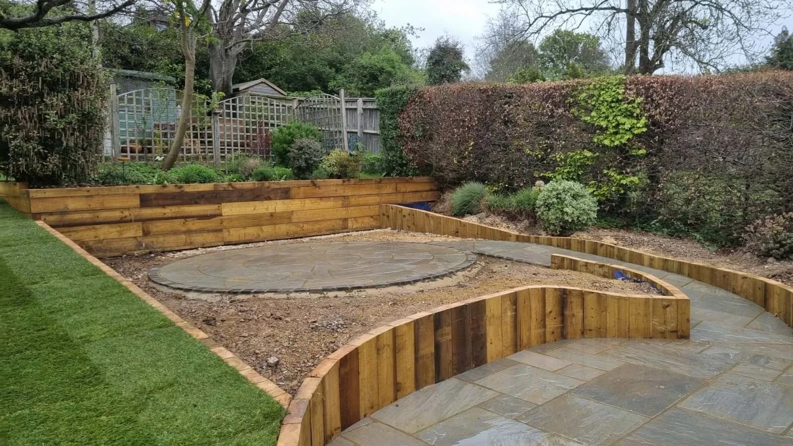 Sleeper-edged terraced garden with a sandstone patio circle and fresh turf